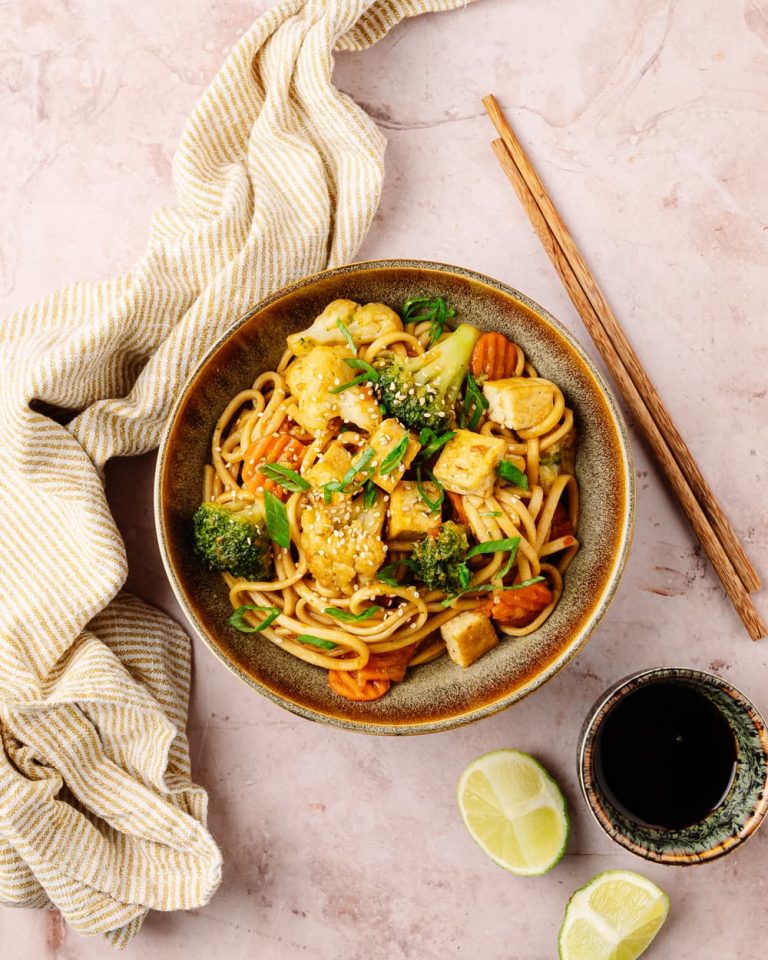 Stir-fry vegano con noodles, tofu dorato e verdure di stagione fotografato dall'alto.